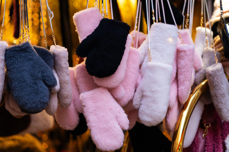 Collection of soft, fluffy winter mittens in shades of pink, black, gray and white, hanging on display in warm, cozy setting with golden light in the backgroundの写真素材