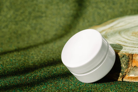 Jar of firming cream with collagen placed on round wooden display on green earthy toned background....