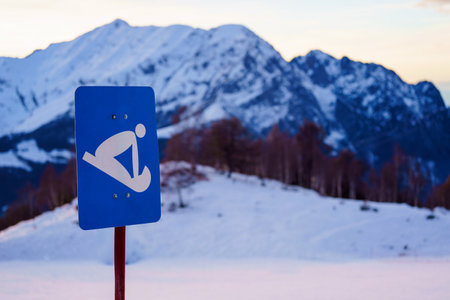 Blue sign indicating sledding, with No Ski No Snowboard written below, stands in front of snow-covered mountain rangeの写真素材