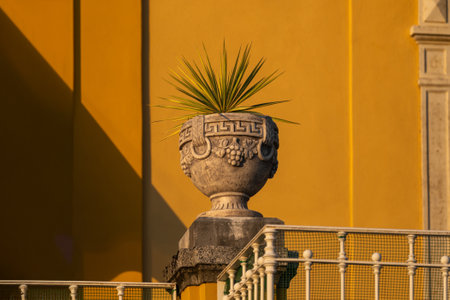 Detailed shot of decorative stone planter with greenery, placed on sunny balcony. The yellow wall and striped awning create warm, Mediterranean atmosphereの写真素材