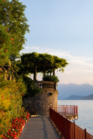 Picturesque lakeside walkway lined with vibrant flowers and lush greenery at Varenna, lake Como, Italy, the serene view at sunset. Mountains and water create stunning backdropの写真素材