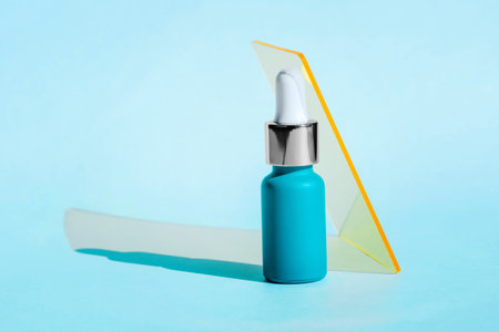 Vibrant blue dropper bottle with white and gold cap stands against light blue background, translucent geometric shape, minimalistic and modern beauty packagingの写真素材
