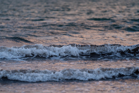 Close-up of gentle waves rolling across the surface of the sea at dusk. The soft lighting reflects off the water, creating peaceful and serene atmosphereの写真素材