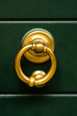 Detailed shot of brass ring door knocker on dark green door. The contrast of golden metal against...