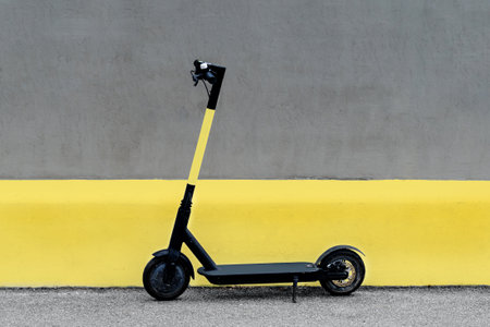 Electric kick scooter in urban environment against wall, scooter rental, freedom of movement. Electric bike in the city. Trendy color of the year 2021. Ultimate grey and illuminating yellow.の写真素材