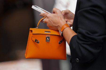 Paris, France - October, 4, 2025: Man wears Hermes orange Birkin bag. Fashion outfit handbag details, street style look accessories, luxury leather accessoryのeditorial素材