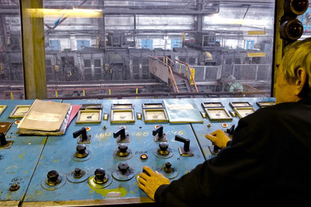 Worker on factory in control room observing the production of steel