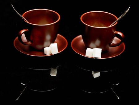 Two tea cups with teaspoons isolated on blackの写真素材