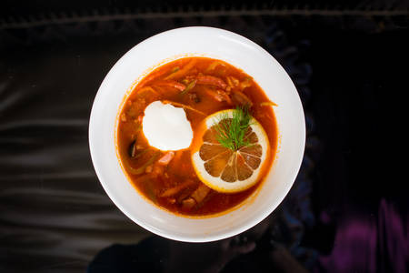 Tasty bowl of red soup with with lemon and sour cream in white plateの写真素材