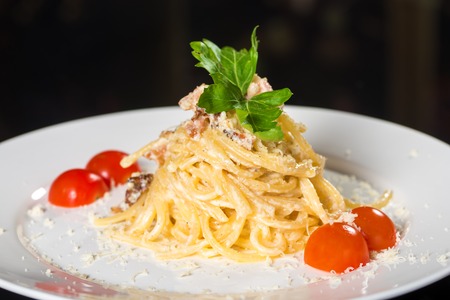 Delicious pasta with mushrooms and tomato on white plate against black backgroundの写真素材