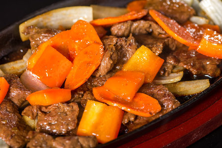 Delicious hot meat with carrots and onions on frying pan on a wooden boardの写真素材