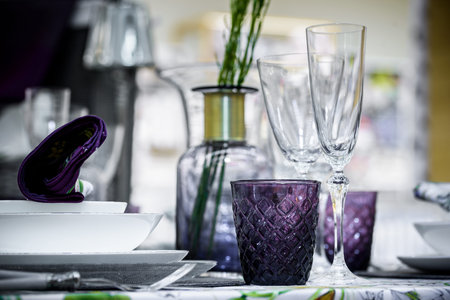 Table serving with decorative tableware. green plants in vase and shiny glasses, plates and bowls on...