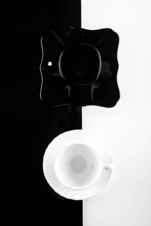 Top view of black and white coffee cups with plates on white and black backgroundの写真素材