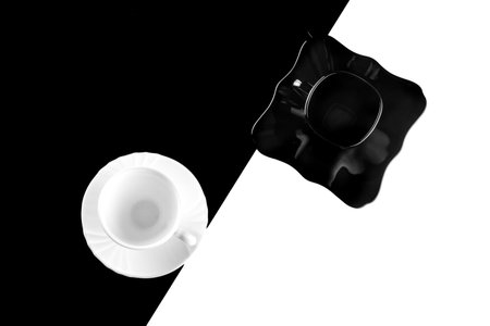 Top view of black and white coffee cups with plates on white and black backgroundの写真素材