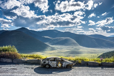Burned car on the mountain road, skyの写真素材