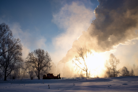Snowy frozen landscape on sunrise with trees and smoke of factoryの写真素材