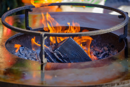 Closeup photo of round steel brazier (grill) with open fire.