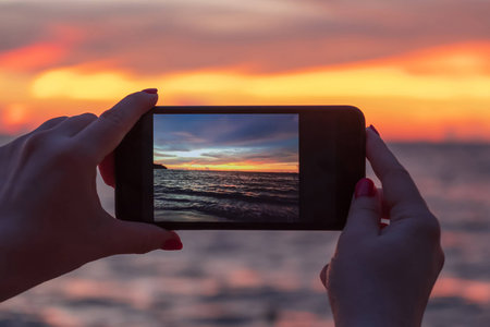 Tourist is holding in hands a smartphone and taking pictures of a colorful and beautiful sunset on theの写真素材