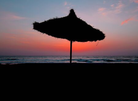 Umbrella on the sea beach on a colorful sunset background.の写真素材