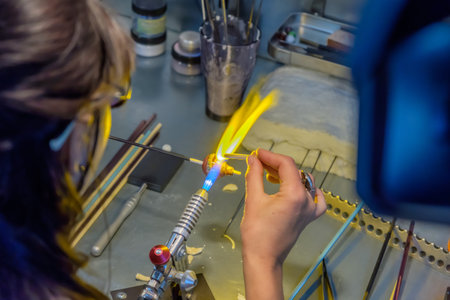 Woman glass artist in her work, with fire torch and tools make decoration.