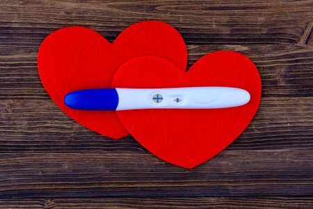 Photo of positive results pregnancy test with red hearts on wooden backgrounds.の写真素材