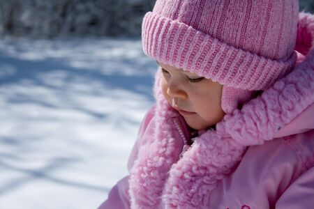 Young girl dressed in pink hat and coat outside in the snow.の写真素材