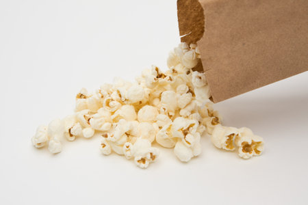 popcorn poured from brown paper bag on white backgroundの写真素材