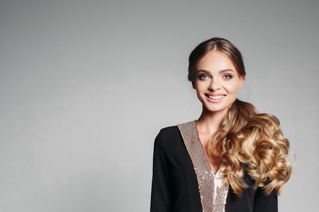 Beautiful, sweet blonde with wavy hair, in an elegant designer suit. Friendly, smiling happily. Look at the camera Isolate on a gray background.の写真素材