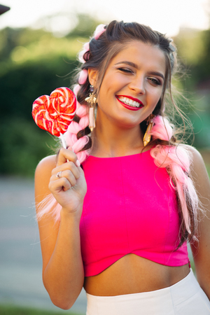 Pretty and positive girl in pink top holding candy heart on stick.の写真素材