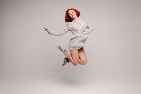 Happy girl with ginger hair jumping in studio with grey background.
