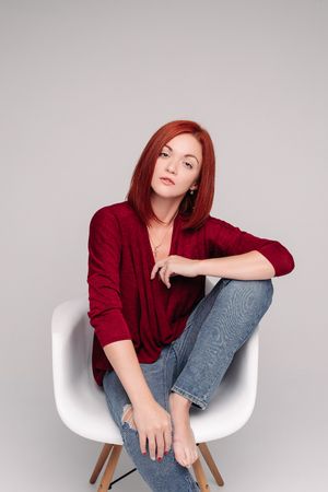 Model with ginger hair sitting on white chair in studio.の写真素材