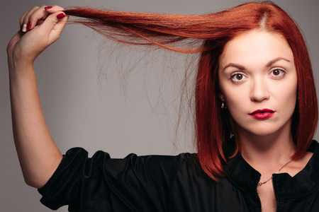 Serious girl with ginger hair holding lock of hair in hand.の写真素材