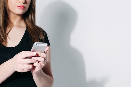 Crop studio shot of brunette young woman in black t-shirt chatting over mobile phone over white background.の写真素材