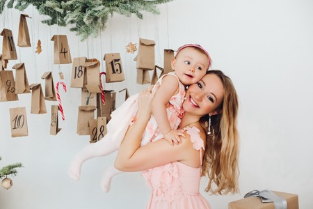 Beautiful mom with little daughter in pink dresses  playing near Christmas decoration.の写真素材