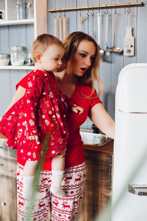 Mom holding by hand little daughter , showing and looking inside refrigerator.の写真素材