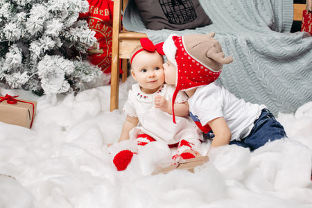 Brother in deer Christmas hat kissing his younger sister in head