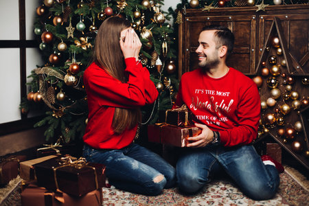 Happy man covering his girlfriends eyes at Christmas.