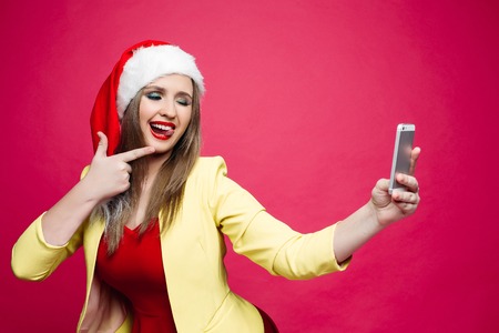 Surprised woman in santa hat making selfie over pink background.の写真素材