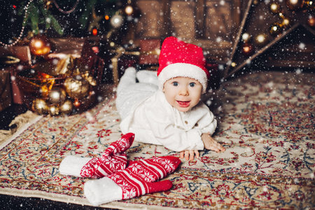 Adorable happy baby in red hat on carpet with cute winter mittens.
