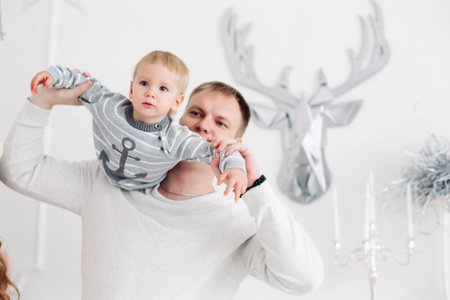 Lovely father keeping son on hands, hugging and kissing him in christmas studio