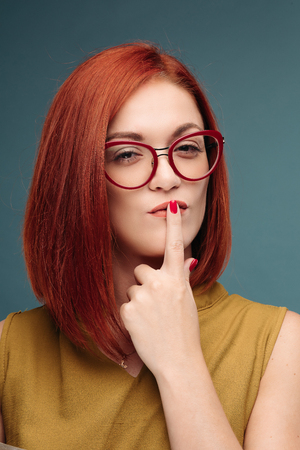 Fashion studio portrait of pretty young hipster red hair woman with bright sexy make up and glasses , wearing stylish urban t shirt, Blue wall backgroundの写真素材