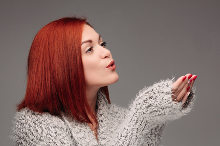 Beautiful young girl with red hair and red nails holding her hands together and blowing on white lightening ball.の写真素材