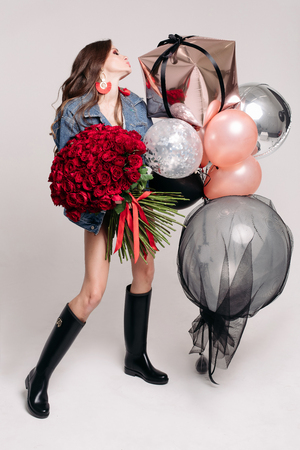Gorgeous stylish brunette woman with bunch of air balloons and red roses.の写真素材