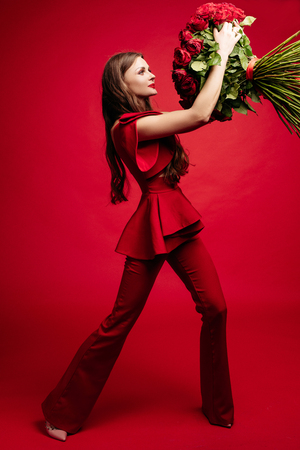 Happy young brunette in red dress holding big bunch of red roses.の写真素材