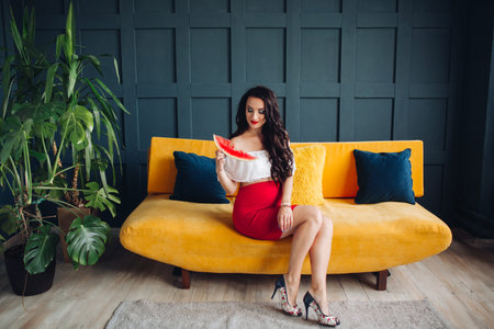 Stylish pregnant woman sitting on orange sofa and posing