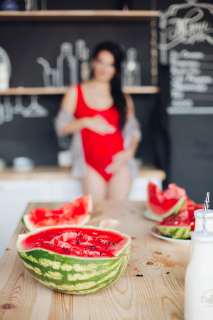 Halved bright watermelon on wooden table against unfocused pregnant woman.の写真素材