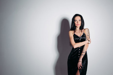 Sensual dark-haired woman in elegant black dress over grey background.