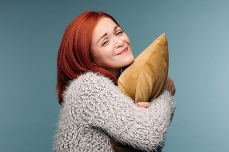 Studio portrait of a woman in a sweater hugging a pillow.の写真素材