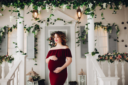 Charming pregnant woman in marsala dress posing on steps of house.