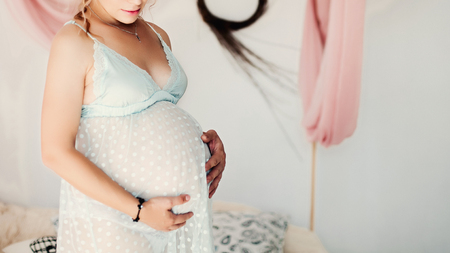 Blonde pregnant woman lying on bedtouching by hands on stomach.の写真素材